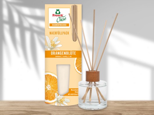 A Frosch Oase glass bottle stands on a table and is filled with water and flowers