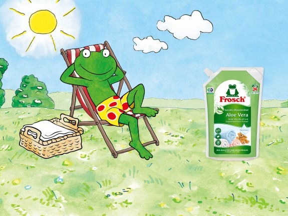Comic frog with deck chair in the grass. Next to it is the Frosch sensitive detergent aloe vera pouch