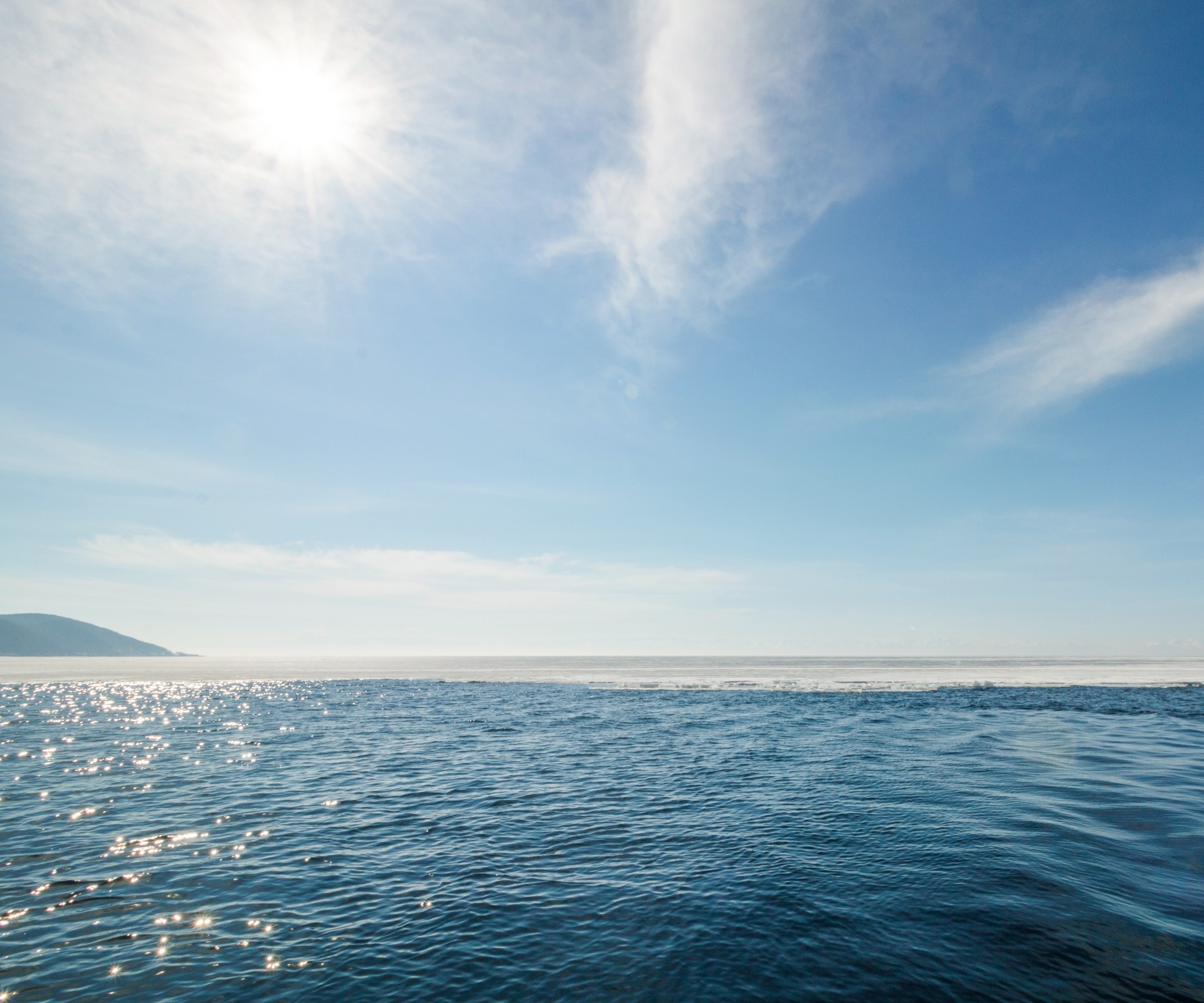 Weitblick auf das Meer mit Sonnenreflexionen und blauem Himmel mit leichten Schleierwolken