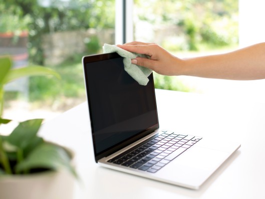 A hand wipes the monitor of a laptop with a cloth