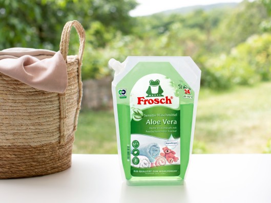 A Frosch sensitive detergent aloe vera pouch stands next to a basket of laundry