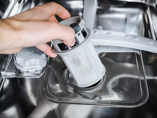 A hand reaches inside a dishwasher and removes the filter