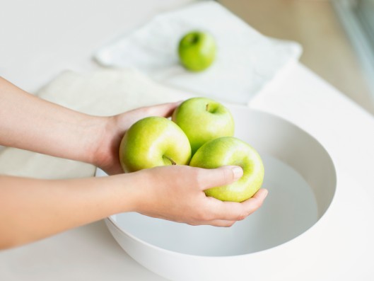 Two hands hold three apples over a bowl of water